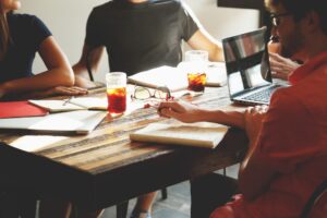 4 people sat meeting around wooden table with documents and a laptop